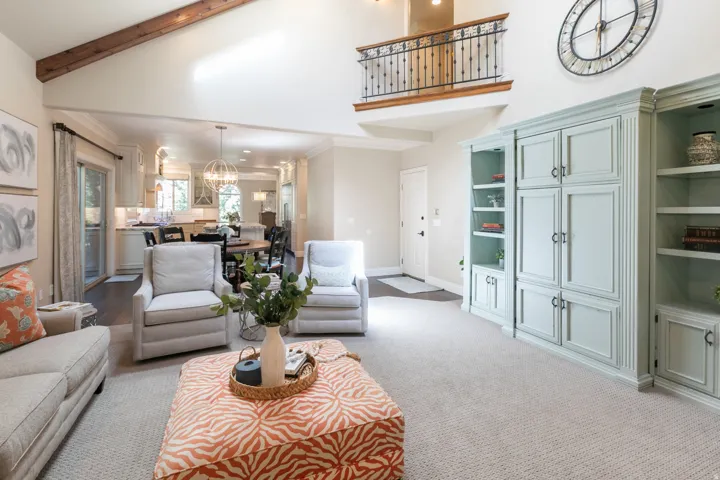 Vaulted ceiling with exposed wood beam, built-in cabinetry with shelving, second-story interior balcony with wrought iron railing, recessed lighting, and wood-finish flooring