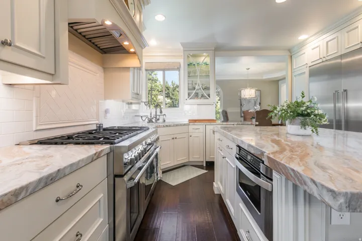 Kitchen featuring wood-finish flooring, custom cabinetry, extensive countertop space, stainless steel range, and built-in microwave