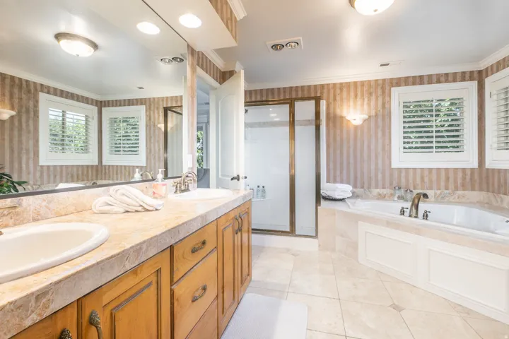 Dual basin vanity with a stone finish countertop, built-in soaking tub, and a glass-enclosed shower