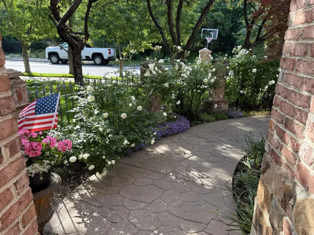 Curved stamped concrete pathway bordered by established landscaping, including flowering shrubs and ground cover