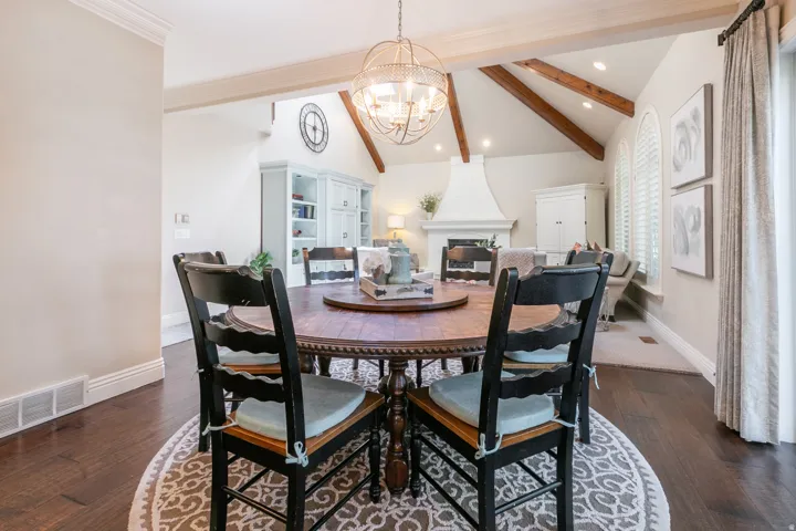 Open concept living space with a vaulted ceiling, exposed wood beams, a prominent fireplace, and two arched windows featuring louvered shutters