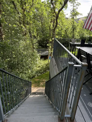 Exterior staircase with metal railings leading to a lower level, surrounded by lush, mature trees