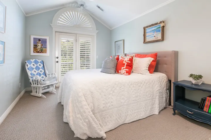 Vaulted ceiling with crown molding, double French doors with plantation shutters, arched transom window, and neutral carpeting