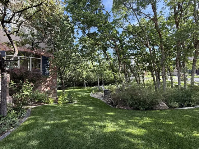 Expansive lawn with mature trees and established landscaping, featuring a brick exterior and a stone-edged garden bed
