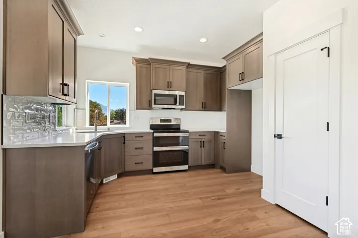 Expansive kitchen featuring wood-finish cabinetry, stainless steel appliances, a white countertop, and a textured tile backsplash