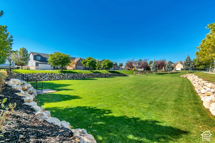 Expansive green space featuring manicured lawn, established rock retaining walls, and mature trees