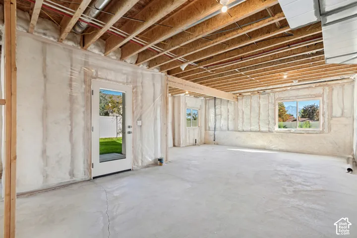 Unfinished lower level featuring exposed wood joists, concrete flooring, exterior-facing door, and multiple windows