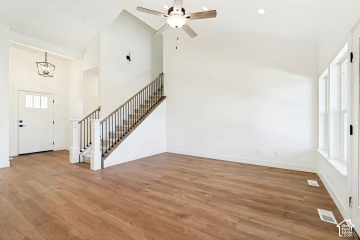 Vaulted ceilings, wood-finish flooring, white paneled door, black geometric pendant light, and a staircase with dark metal balusters