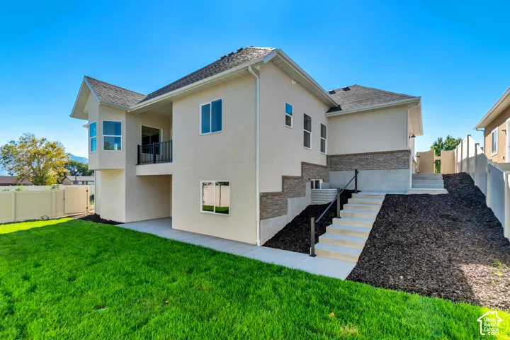 Stucco exterior with brick detailing, a second-story balcony with metal railing, multiple windows, and a concrete patio