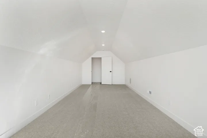 Neutral tone carpeting, recessed ceiling lighting, sloped ceilings, white painted walls, and a white interior door