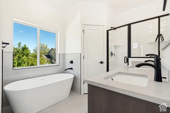 Freestanding soaking tub with wall-mounted faucet, dual vanity with integrated sinks and matte black hardware, and a glass-enclosed shower