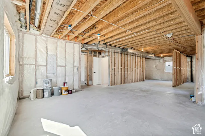 Unfinished basement with exposed ceiling joists, concrete floor, framed interior walls, and windows