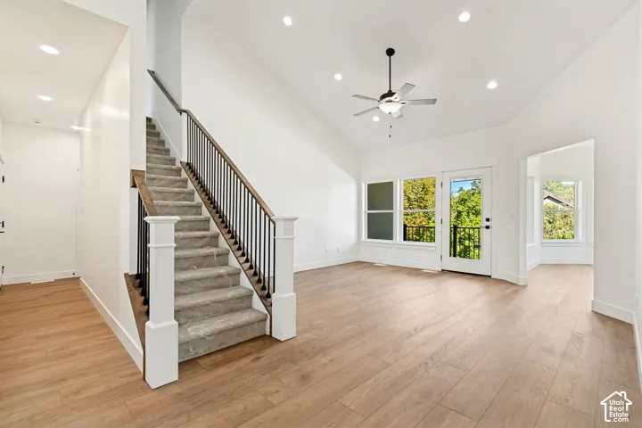 Vaulted ceiling with a ceiling fan, recessed lighting, wood-finish flooring, and a staircase with a black metal railing and wood-finish handrail