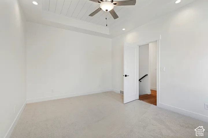 Tray ceiling with shiplap detail, recessed lighting, ceiling fan, white paneled door with matte black hardware, and neutral carpeting