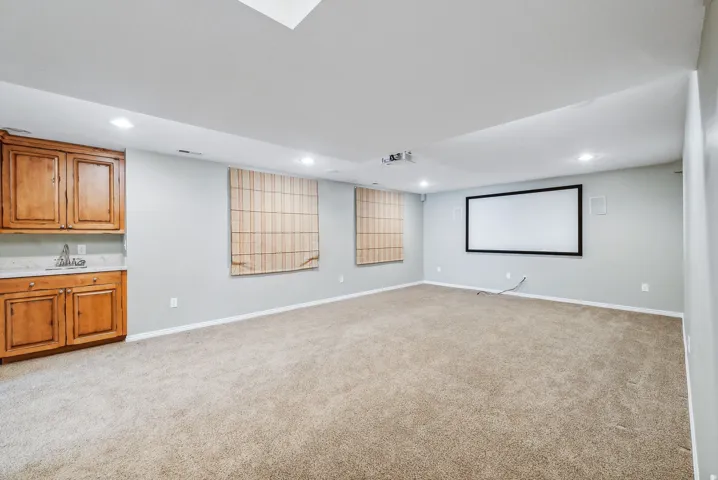 Integrated wet bar with wood cabinetry and stone countertop, built-in projection screen, recessed lighting, and carpeted flooring