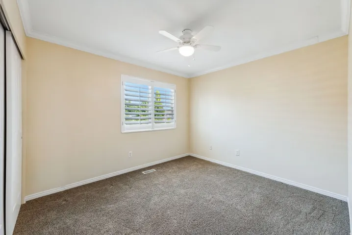 Window with plantation shutters, ceiling fan, crown molding, and wall-to-wall carpeting