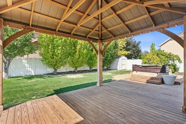 Expansive wooden deck with a built-in hot tub, covered by a wooden gazebo with a corrugated roof
