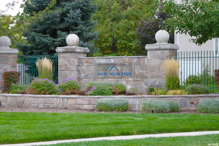 Stone-clad entry columns with spherical finials, an ornate iron fence, and layered landscaping with varied foliage