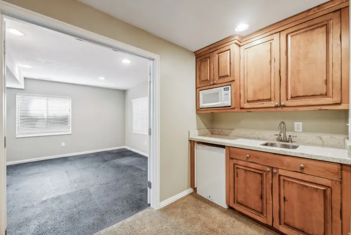 Wet bar featuring wood cabinetry, built-in microwave, compact refrigerator, and undermount sink with a stainless steel faucet