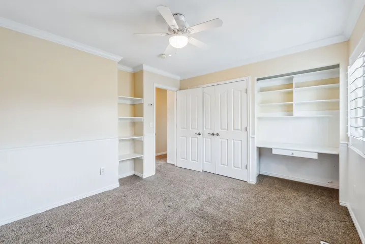 Recessed built-in shelving, built-in desk with shelving, ceiling fan, bi-fold closet doors, and crown molding