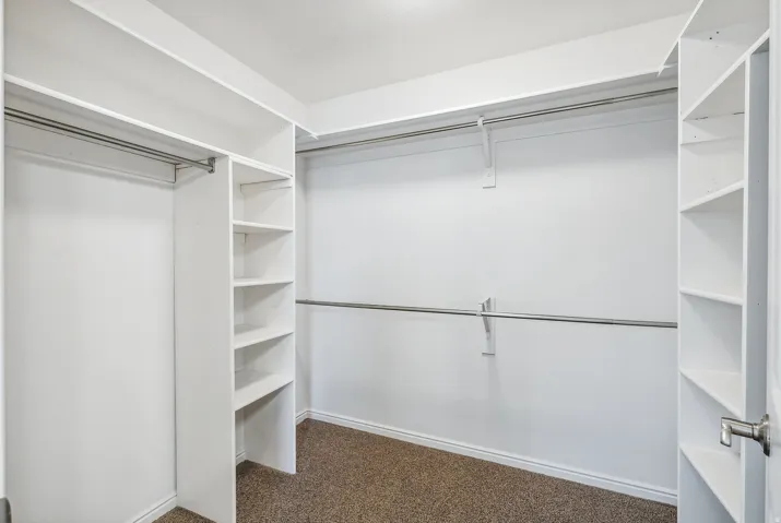 Walk-in closet with integrated shelving units, metal hanging rods, and textured carpet flooring