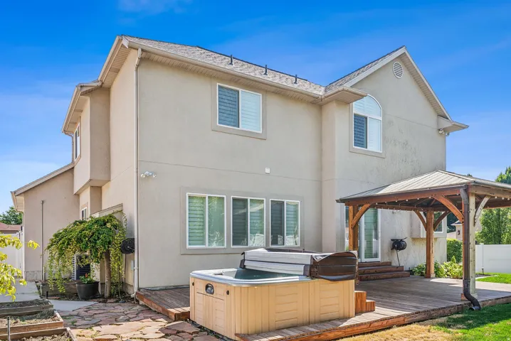 Stucco exterior with multiple windows, an upper arched window, a wooden deck, a hot tub, and an outdoor gazebo with a metal roof