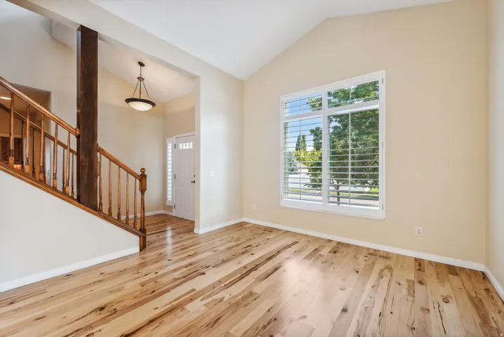 Vaulted ceiling, wood-finish flooring, staircase with wood railing, window with plantation shutters, and a front entry door with side-lite