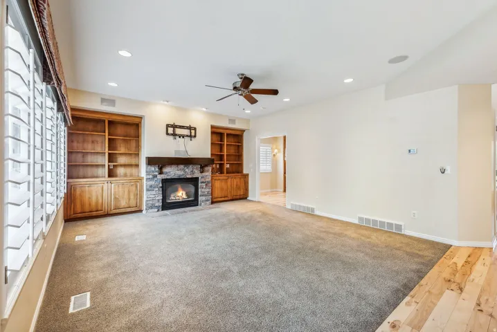 Living space featuring a stone-surround fireplace, built-in wooden shelving, recessed lighting, ceiling fan, and wood-finish flooring