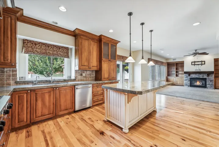 Wood-finish flooring, built-in wooden cabinetry, recessed lighting, stone fireplace with a wooden mantel, and a kitchen island with pendant lighting