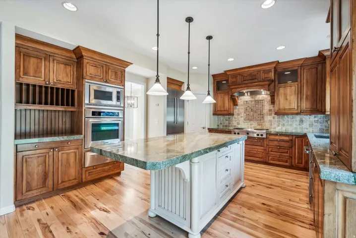Wood-finish flooring, white kitchen island with an extended counter, stainless steel double oven, stainless steel microwave, and wood cabinetry throughout