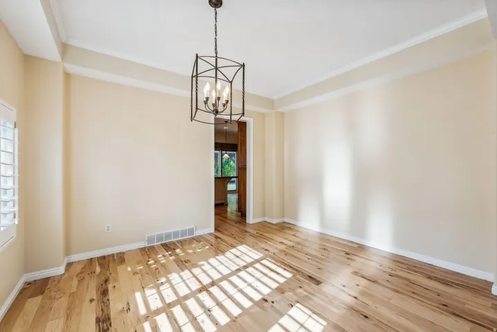 Tray ceiling with crown molding, wood-finish flooring, plantation shutters, and a chandelier