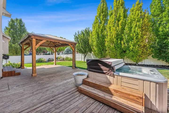 Expansive backyard deck with an attached wooden pergola, integrated hot tub, and a white privacy fence