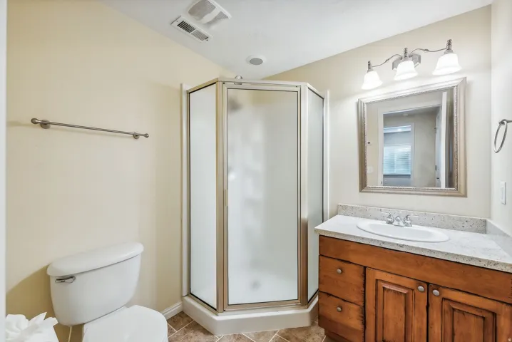 Bathroom featuring a corner shower, single vanity with light-toned countertop, wood-finish cabinetry, and a framed mirror