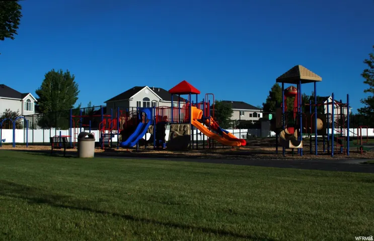 Expansive grassy area with a multi-level play structure featuring slides, climbing elements, and protective ground covering