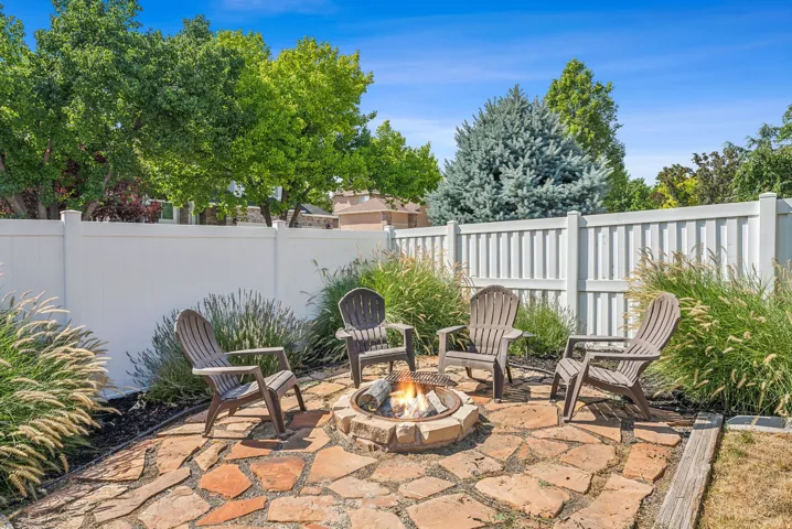 Flagstone patio with a built-in fire pit, surrounded by lush ornamental grasses and a white privacy fence
