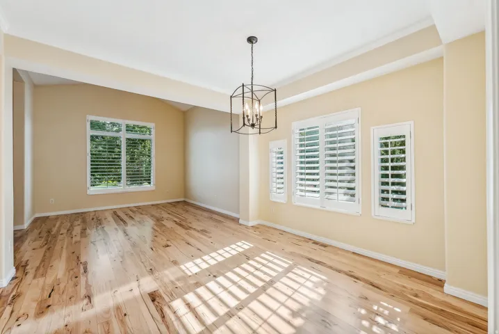 Wood-finish flooring with a satin finish, white plantation shutters, decorative ceiling light fixture, and arched ceiling detail