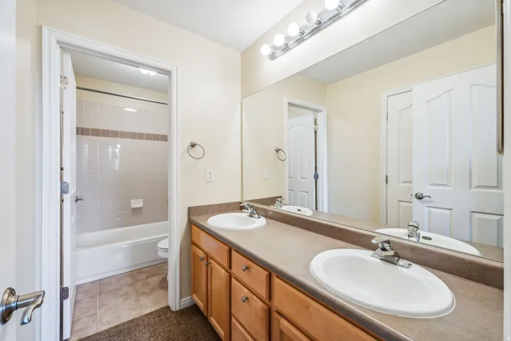 Dual vanity with integrated sinks, wood-finish cabinetry, a full-width mirror, and overhead strip lighting