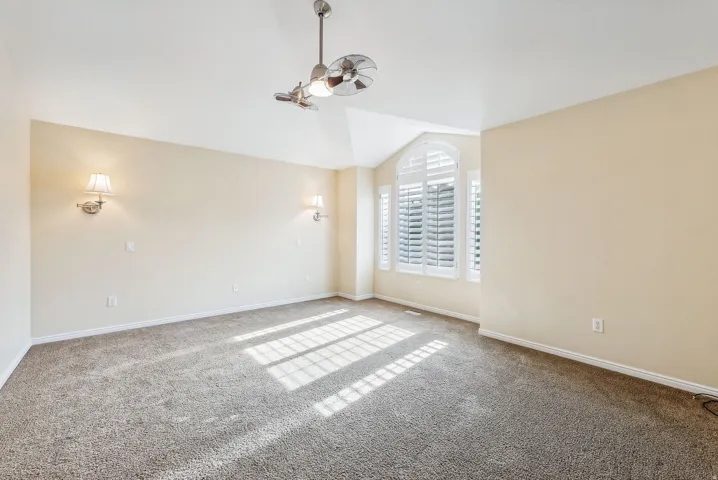 Vaulted ceiling with a ceiling fan, arched windows featuring plantation shutters, and wall-mounted sconce lighting