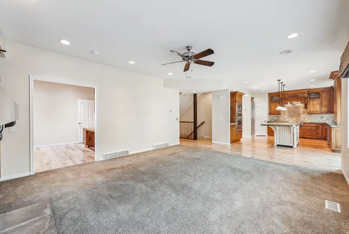 Expansive carpeted living area featuring recessed lighting, a ceiling fan, and an open doorway to another room with wood-finish flooring