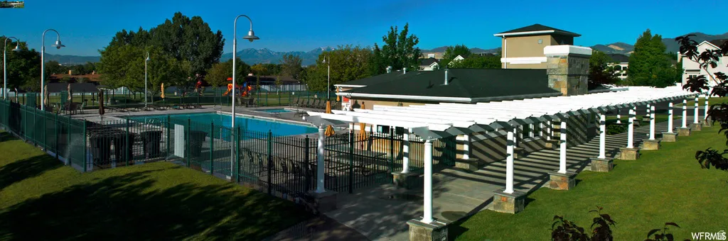 Outdoor swimming pool with a surrounding wrought iron fence, adjacent to a structured pergola walkway