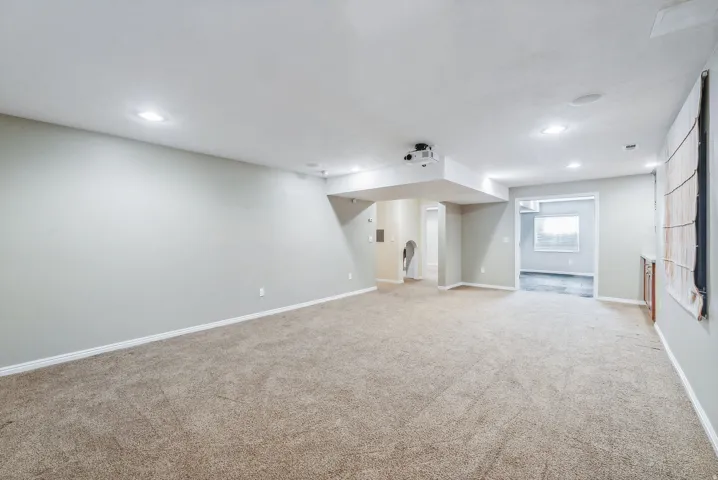 Expansive carpeted room featuring recessed lighting, a ceiling-mounted projector, and neutral wall tones