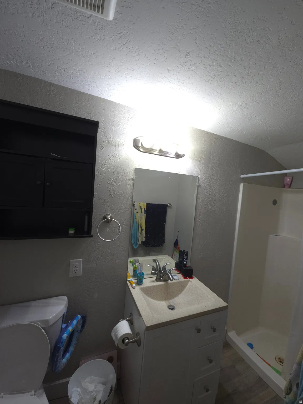 Bathroom featuring a vanity with an integrated sink, a built-in shower, and a wall-mounted storage cabinet