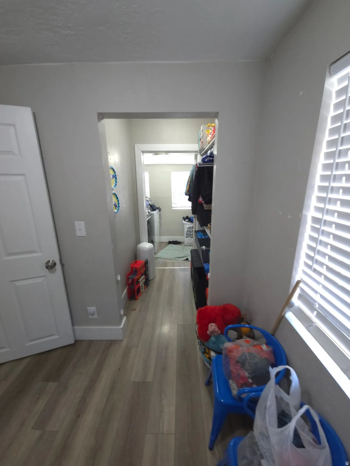 Wood-finish flooring throughout, white interior door, and window with horizontal blinds