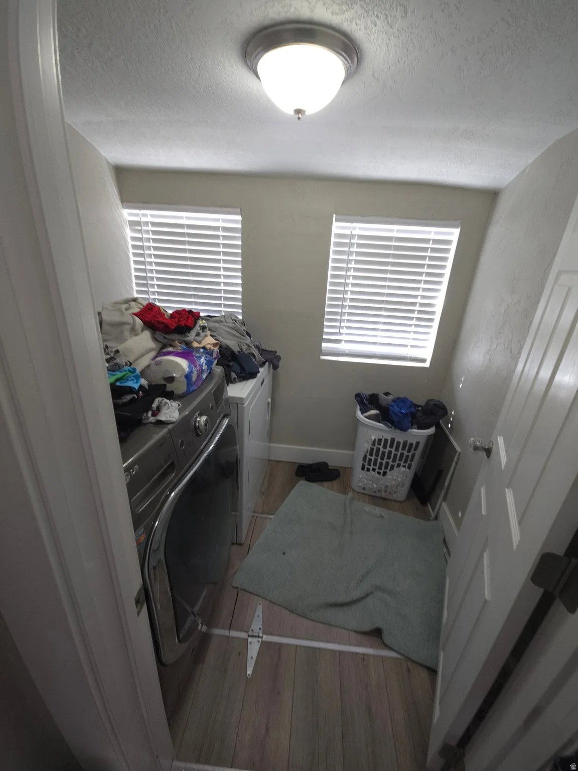 Laundry area featuring wood-finish flooring, two windows with blinds, and a flush mount ceiling light fixture