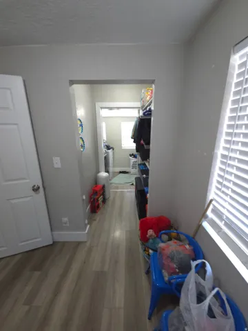 Wood-finish flooring throughout, white interior door, and window with horizontal blinds