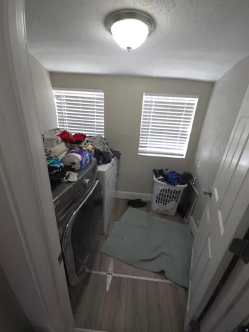 Laundry area featuring wood-finish flooring, two windows with blinds, and a flush mount ceiling light fixture
