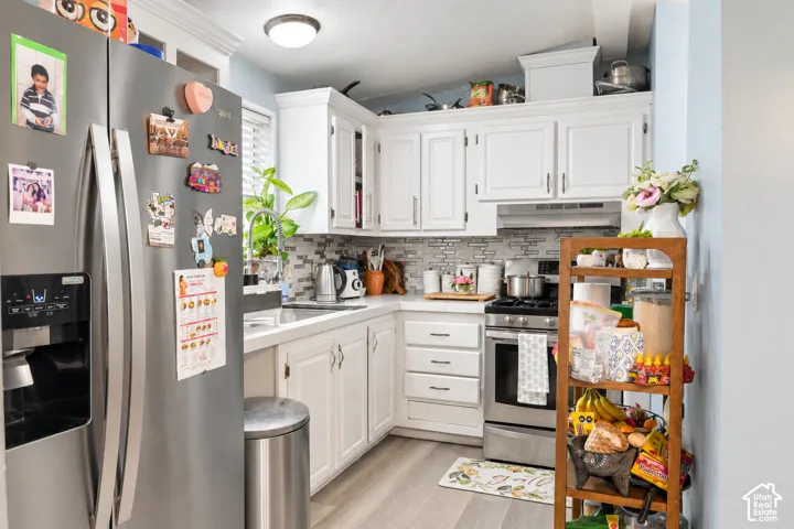 White cabinetry, stainless steel appliances, light wood-finish flooring, mosaic tile backsplash, and a flush mount ceiling light fixture