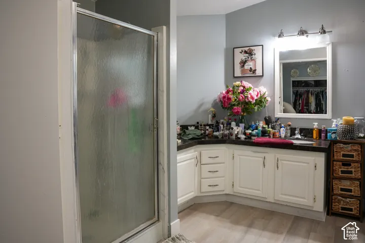 Frosted glass shower enclosure, vanity with white cabinetry, dark countertop, single basin sink, and wood-finish flooring