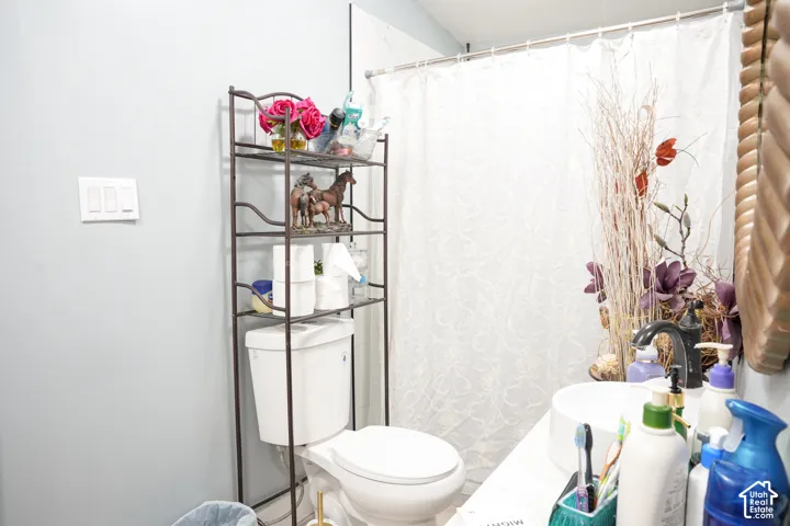 White toilet with an overhead shelving unit, a white vanity with a vessel sink, and a dark-finish faucet