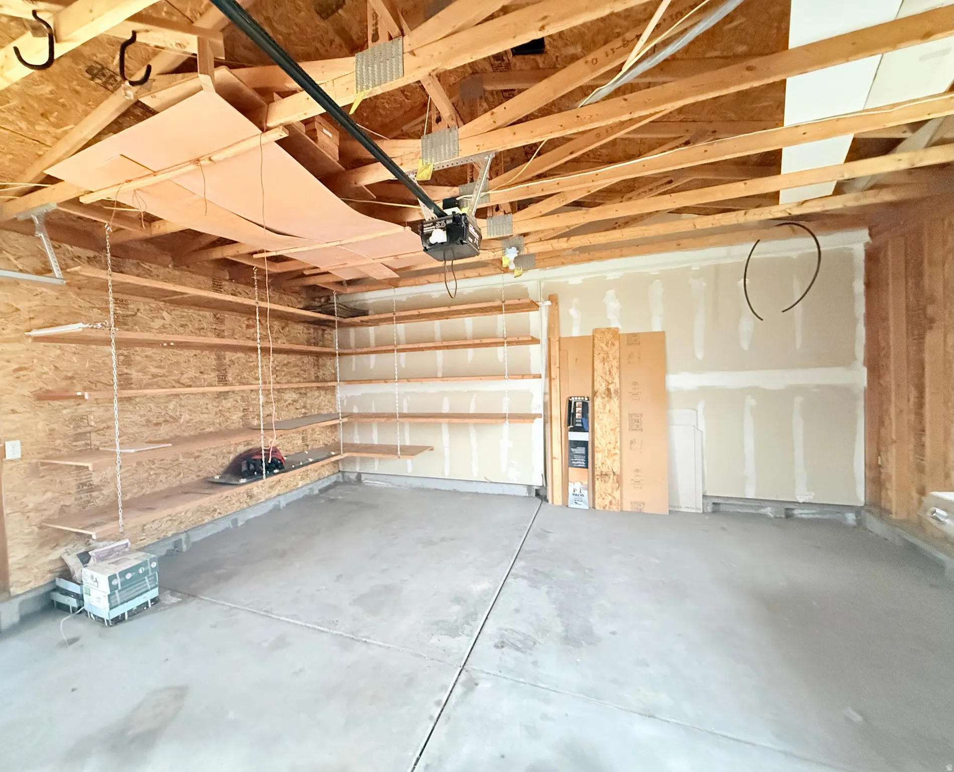 Attached garage featuring exposed ceiling joists, concrete flooring, and built-in wood shelving along two walls